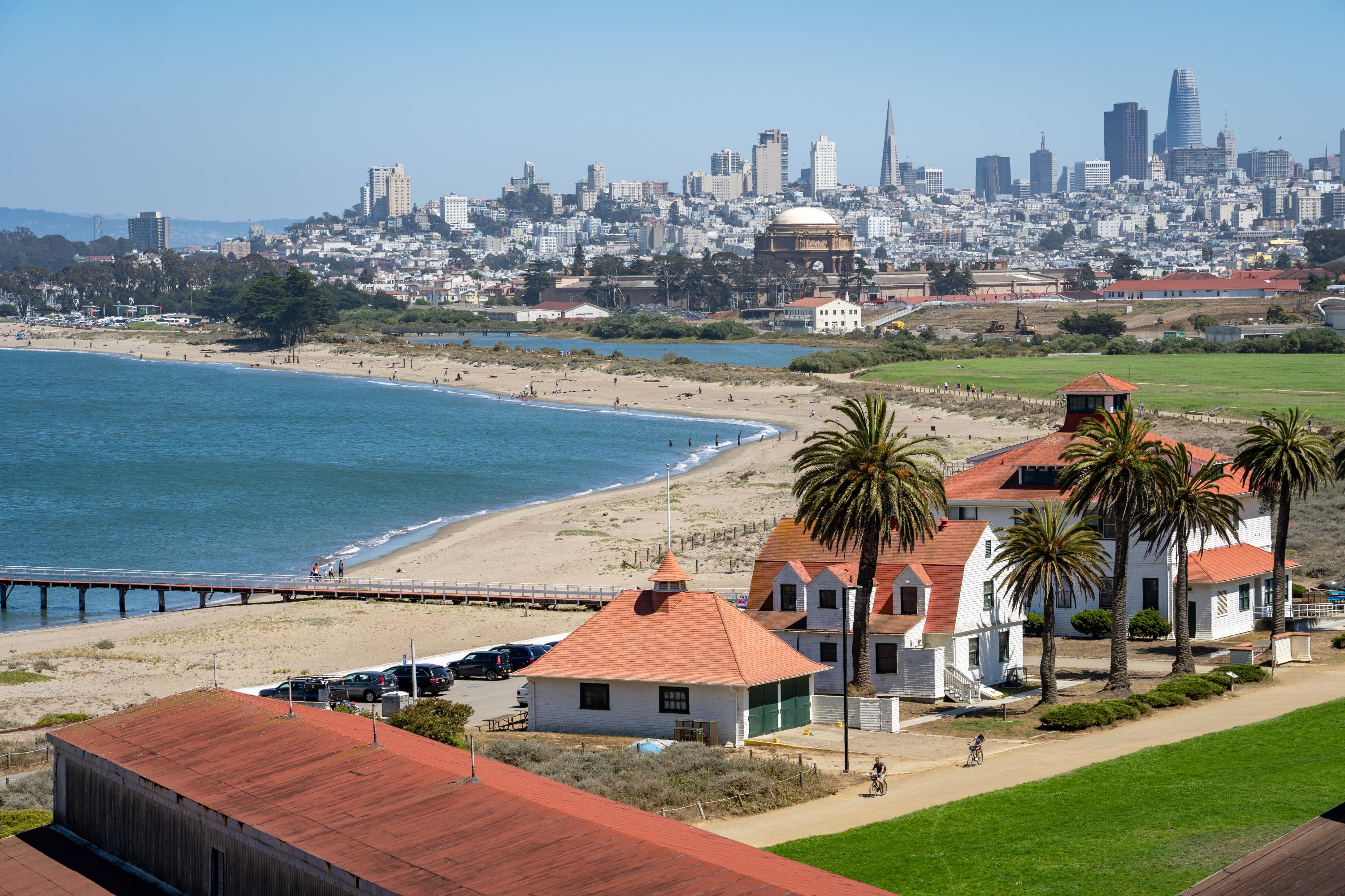 view looking southwest across the beach and wetlands at crissy field. A few buildings and a pier sit in the foreground, the skyline of San Francisco is visible in the background.