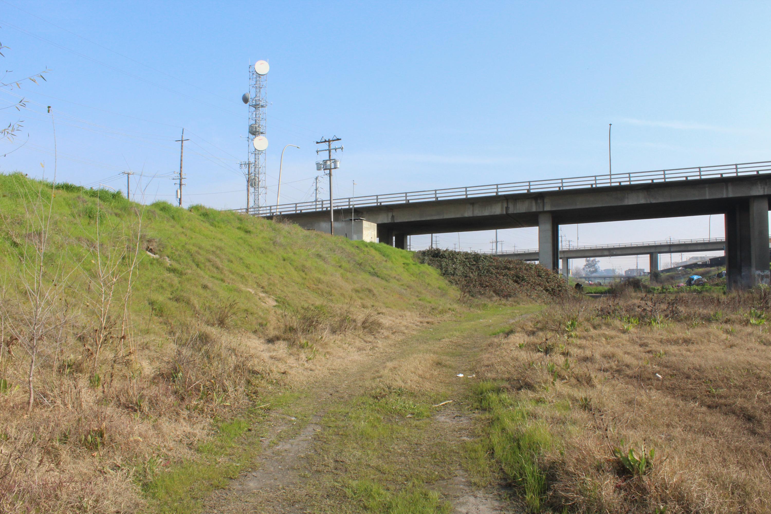 Looking down the grass covered dry slough under an overpass.