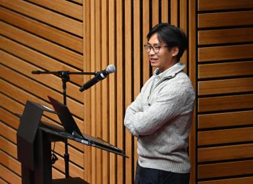 Martin Trinh smiles and stands behind the podium with arms folded.
