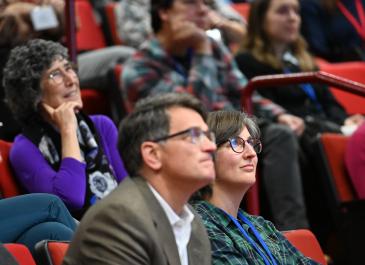 Kayli Paterson looks up towards the front of the room. Matthew Heberger and Kelly Moran are in partial focus and are looking the same direction.