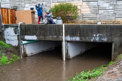 Two scientists on bridge with sampling equipment over muddy culvert