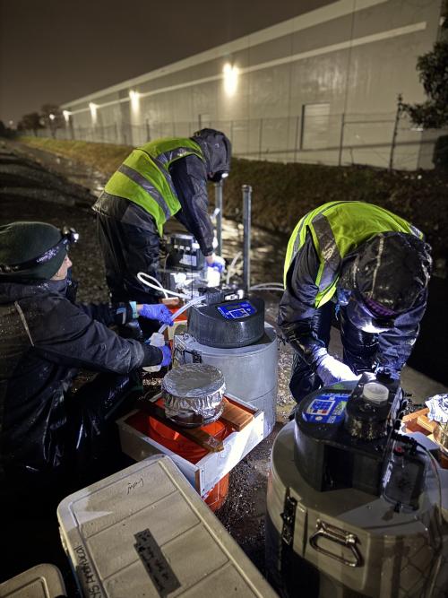 Scientists in rain gear run sampling machines along a paved path in the dark