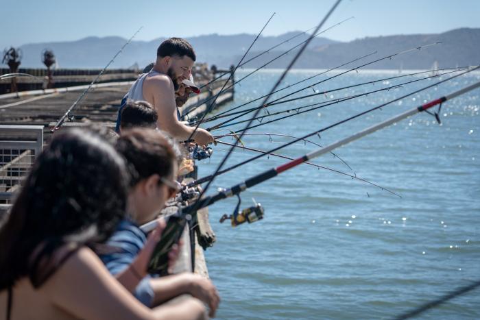 Lots of people fishing with rods along pier.