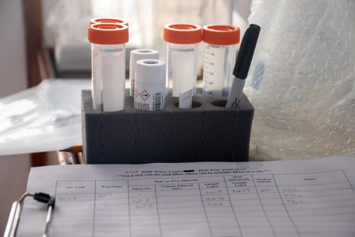 Vials of different sizes and a sharpie positioned upright behind an out of focus clipboard with a data table