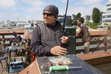 Smiling Anthony Khalil baits a hook during a morning fishing session at Mission Rock pier.