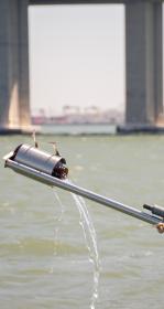 Water falling from a bottle attached to the end of a long pole into San Francisco Bay below Bay Bridge