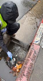 Scientist in rain gear crouches beside open storm drain