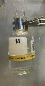 Glass bottle with clear liquid displaying yellow "contaminant" label