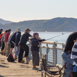 People of all ages fishing with rods off a wooden dock