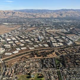 Aerial view showing suburban housing in Santa Clara and industrial buildings in San Jose, separated by the Ulistac Natural Area along the Guadalupe River
