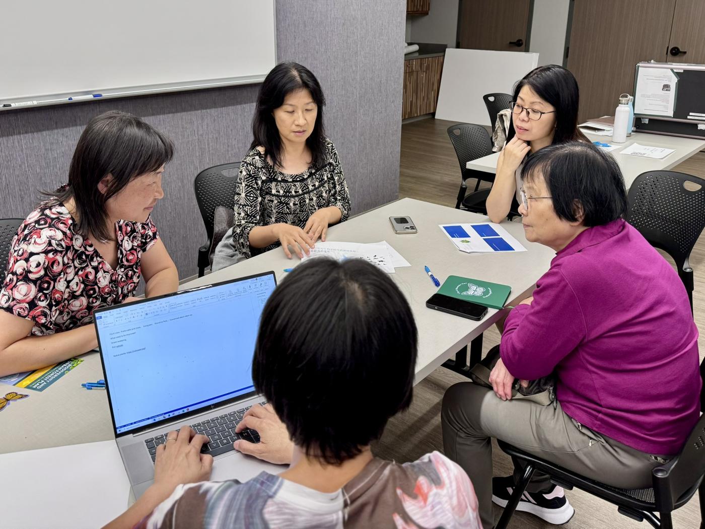 A group of women sit around a desk talking and looking at documents together.
